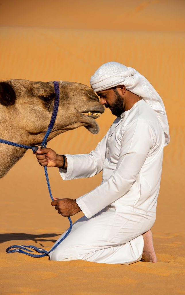 a man in a white outfit is petting a camel