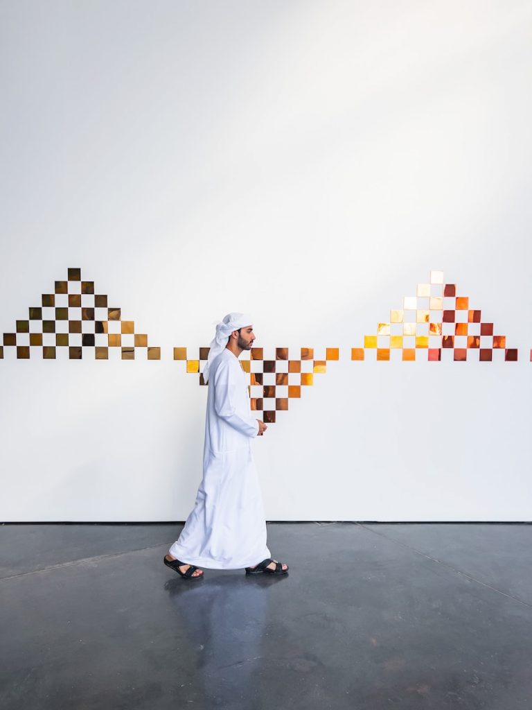 a man in a white outfit is walking in front of a checkered wall